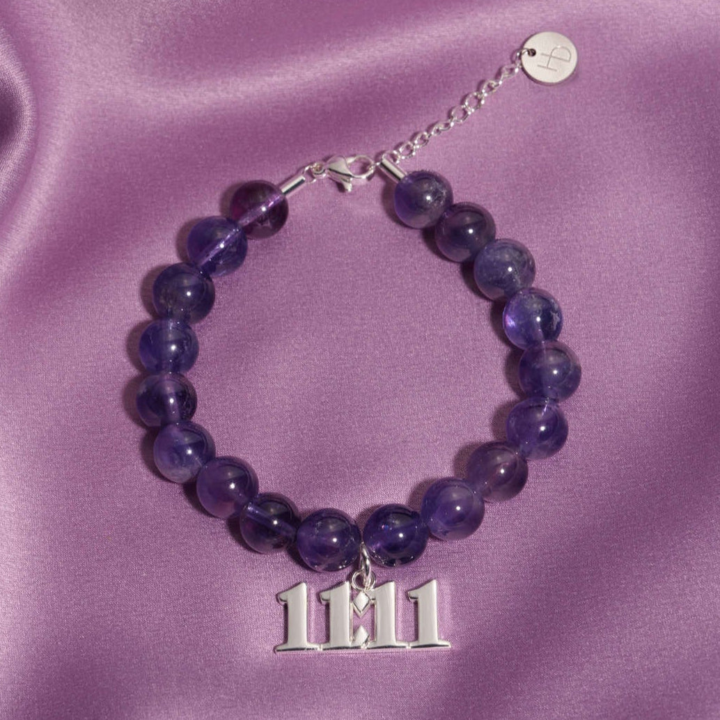 11:11 Silver charm on beaded amethyst bracelet laying on silk