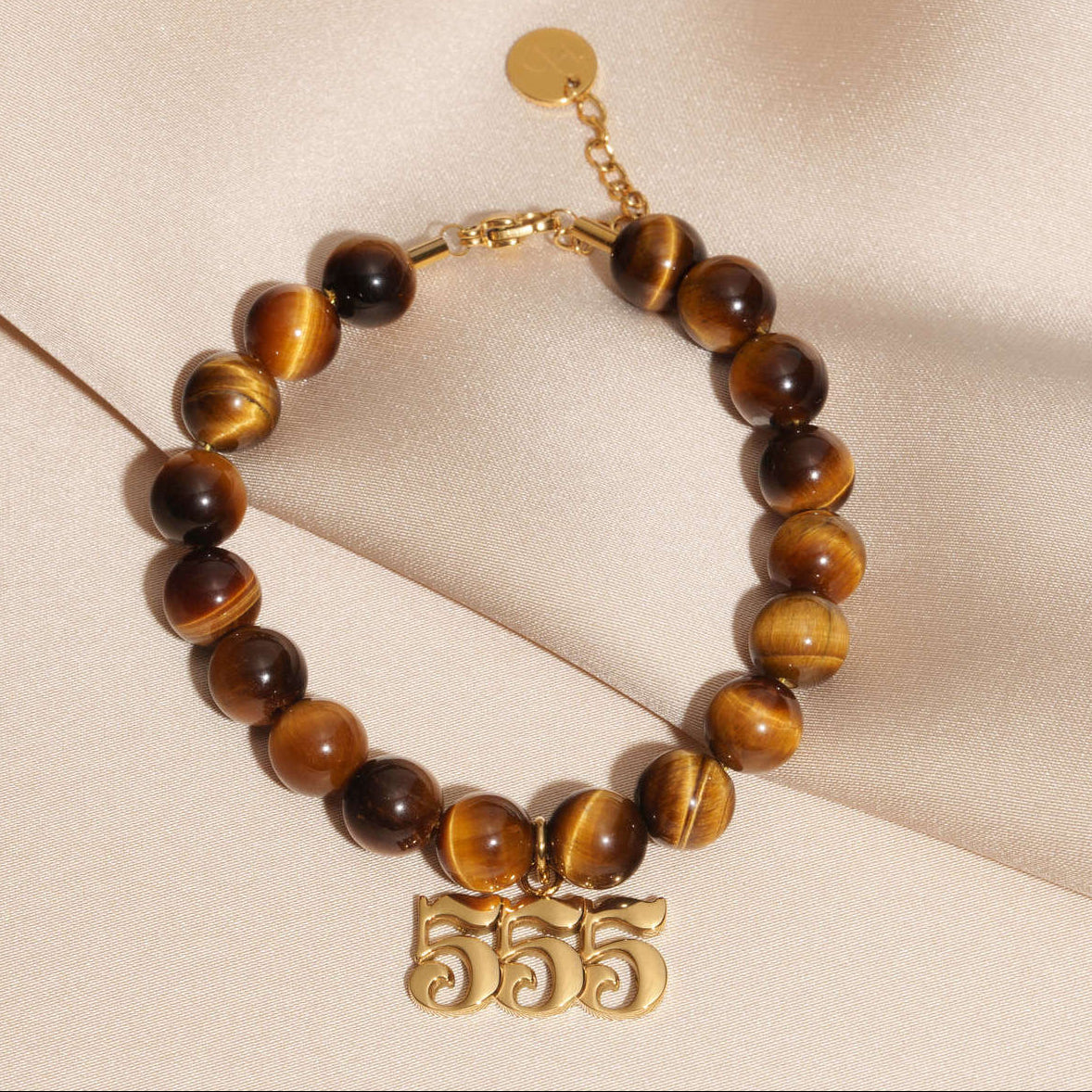 555 Gold charm on beaded Tigers Eye bracelet laying on silk