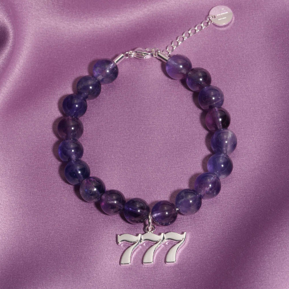 777 silver charm on beaded amethyst bracelet laying on silk