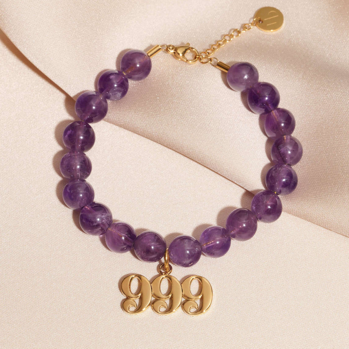 999 gold charm on beaded amethyst bracelet laying on silk