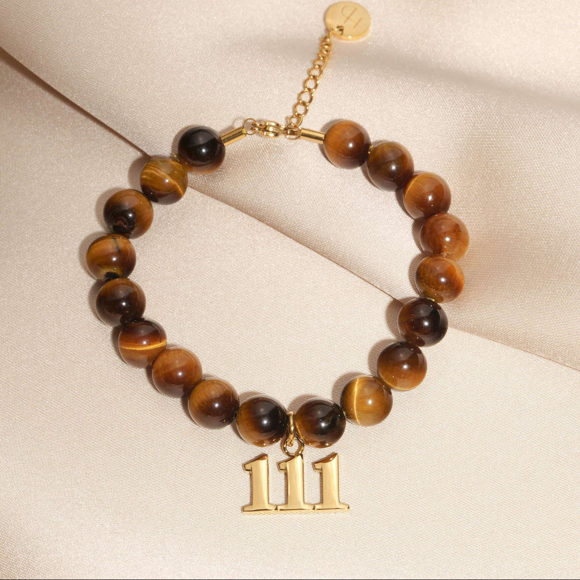 111 Gold charm on beaded Tigers Eye bracelet laying on silk
