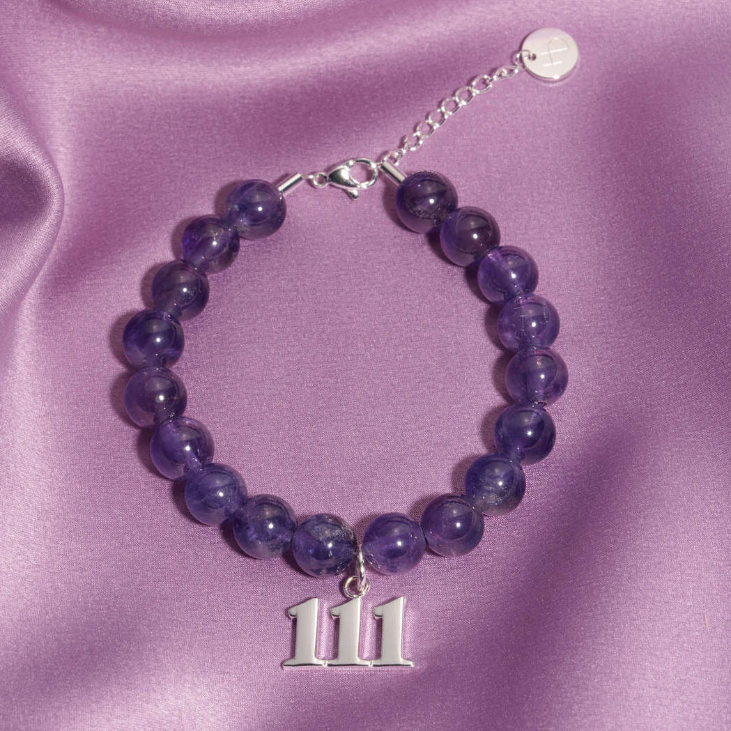 111 Silver charm on beaded amethyst bracelet laying on silk
