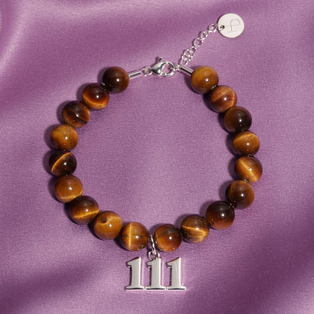 111 Silver charm on beaded Tigers Eye bracelet laying on silk
