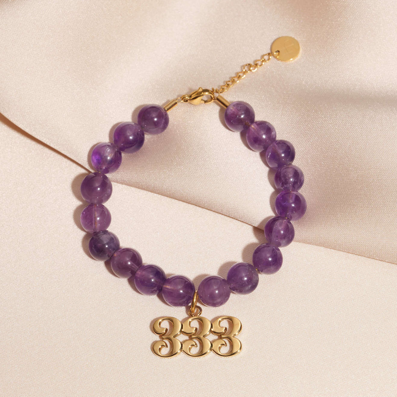 333 gold charm on beaded amethyst bracelet laying on silk
