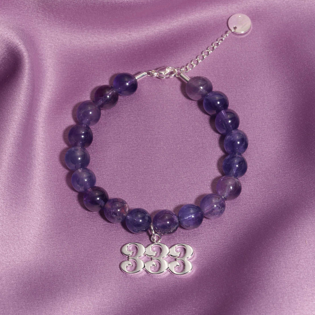 333 Silver charm on beaded amethyst bracelet laying on silk
