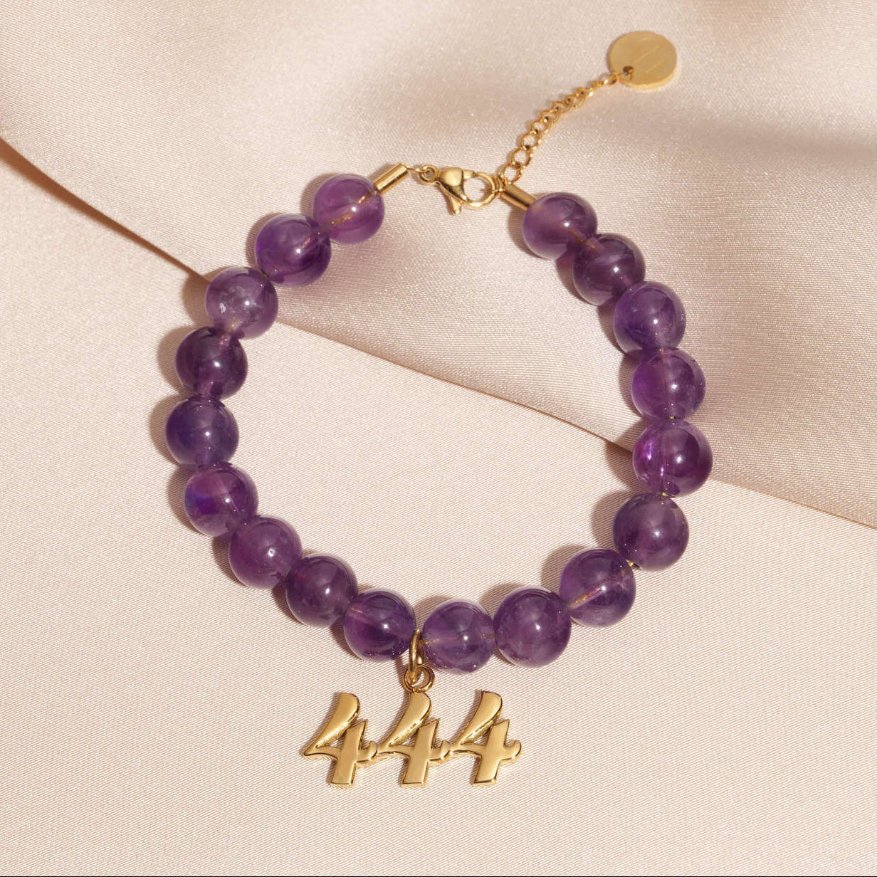 444 gold charm on beaded amethyst bracelet laying on silk
