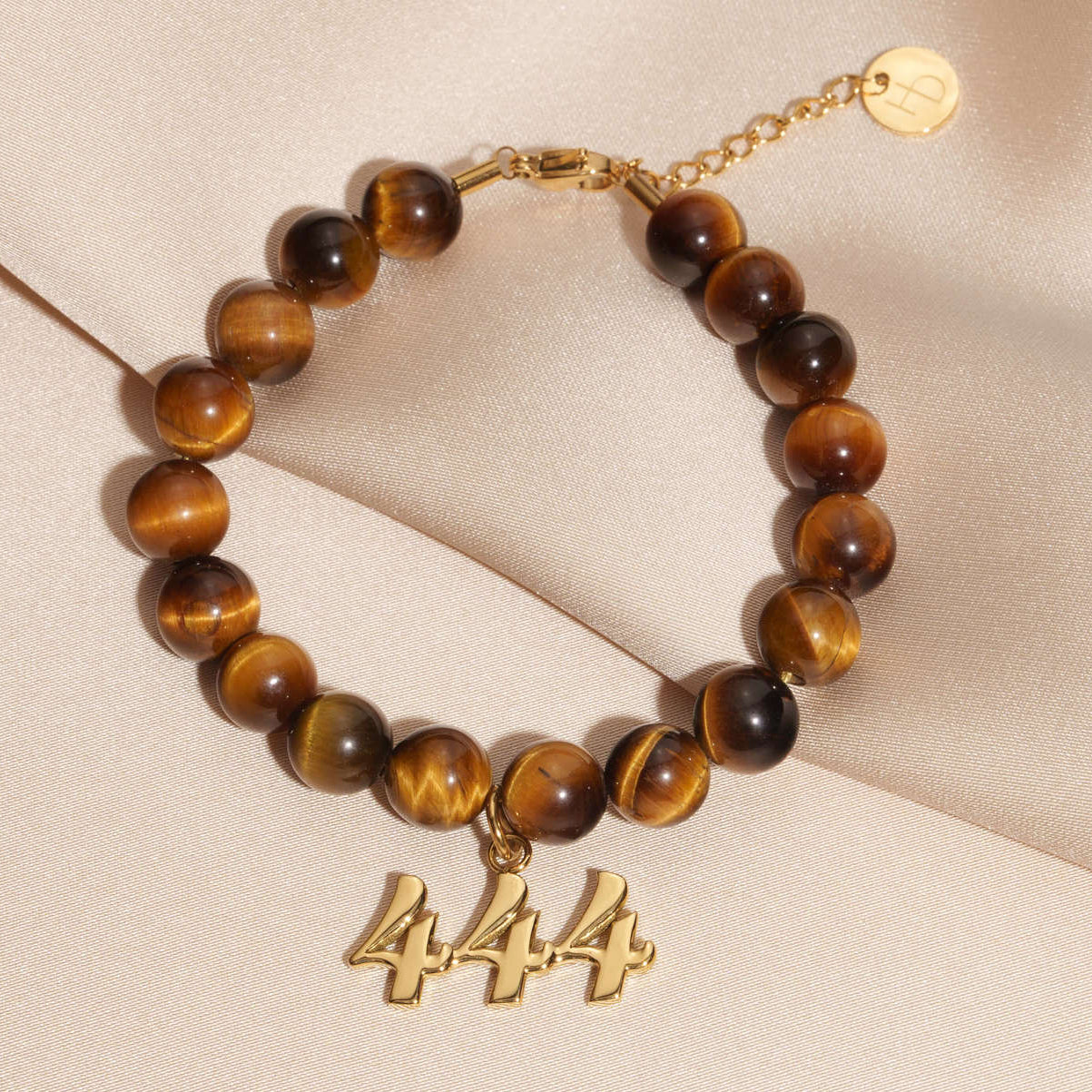 444 Gold charm on beaded Tigers Eye bracelet laying on silk
