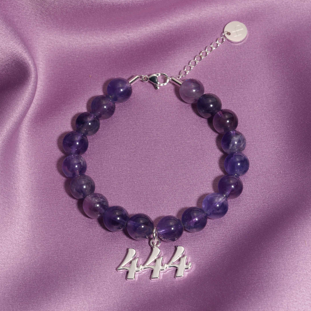 444 silver charm on beaded amethyst bracelet laying on silk
