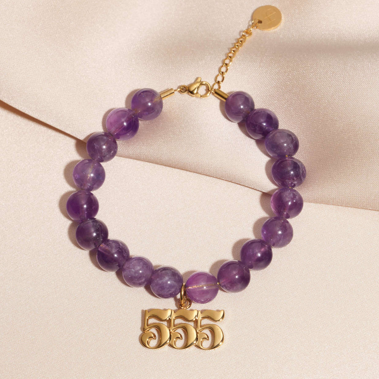 555 gold charm on beaded amethyst bracelet laying on silk
