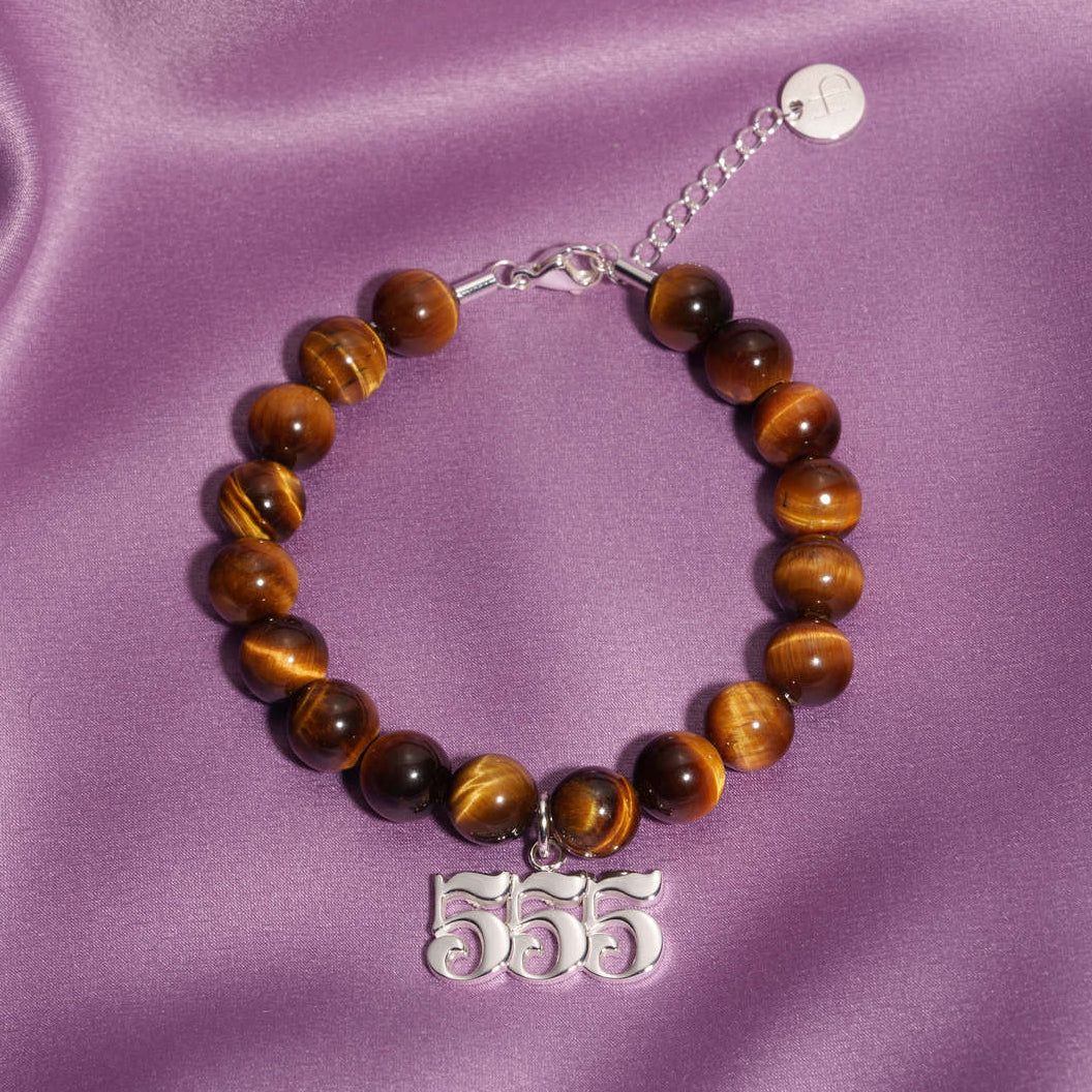 555 Silver charm on beaded Tigers Eye bracelet laying on silk
