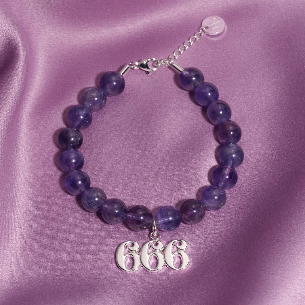 666 silver charm on beaded amethyst bracelet laying on silk
