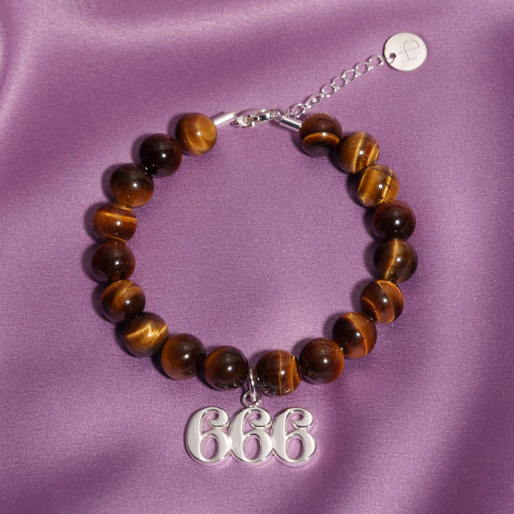666 Silver charm on beaded Tigers Eye bracelet laying on silk
