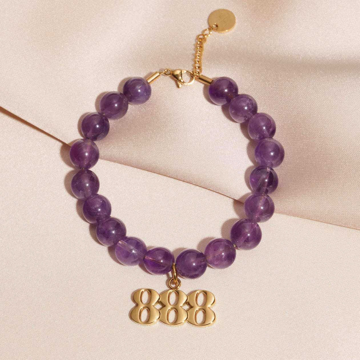 888 gold charm on beaded amethyst bracelet laying on silk
