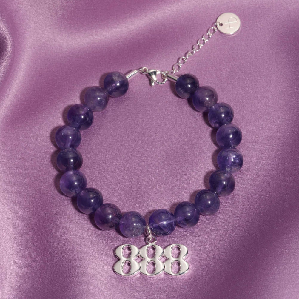 888 Silver charm on beaded amethyst bracelet laying on silk
