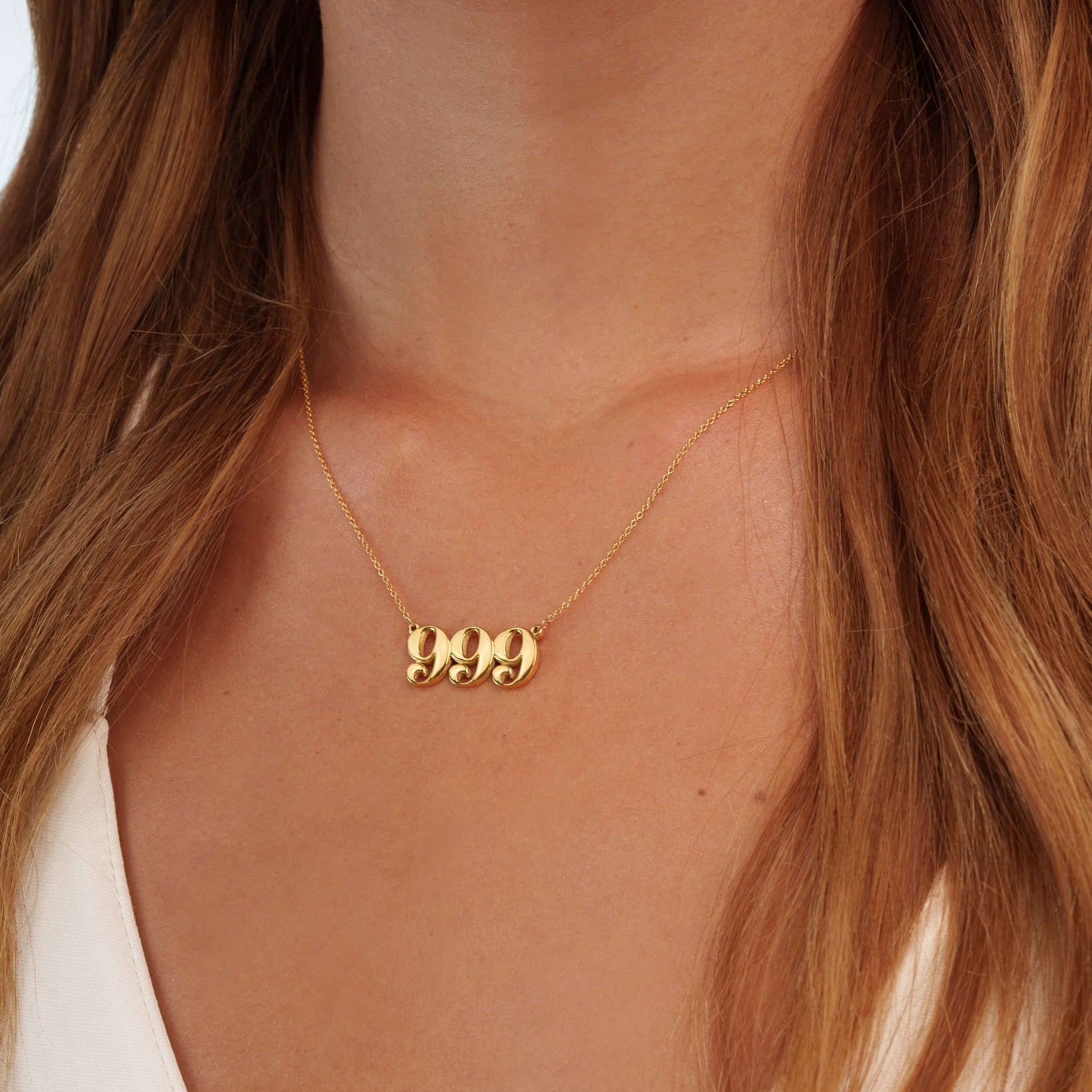 Gold necklace with '999' pendant on a person with long hair